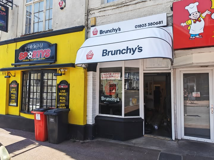 Brunchy's Takeaway storefront on Belgrave Road, Torquay showing white awning with takeaway name and phone number, red chef character sign, and large windows